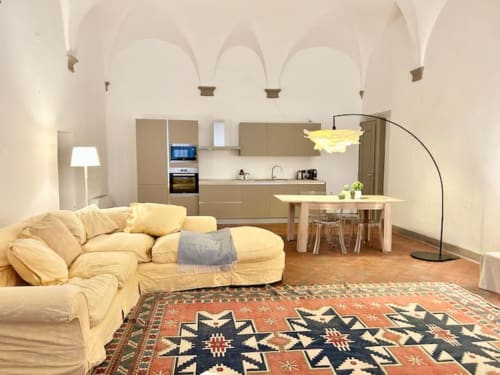 Ampio appartamento bolognese con divano color crema, tappeto geometrico, cucina a vista e soffitti a volta nel palazzo storico