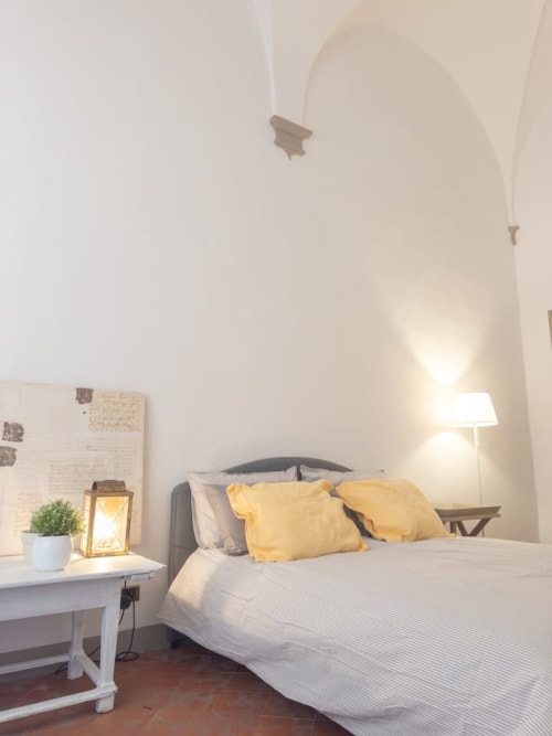 Camera luminosa in Living Palazzi Storici Bologna con soffitto a volta, cuscini gialli, scrivania bianca e illuminazione calda