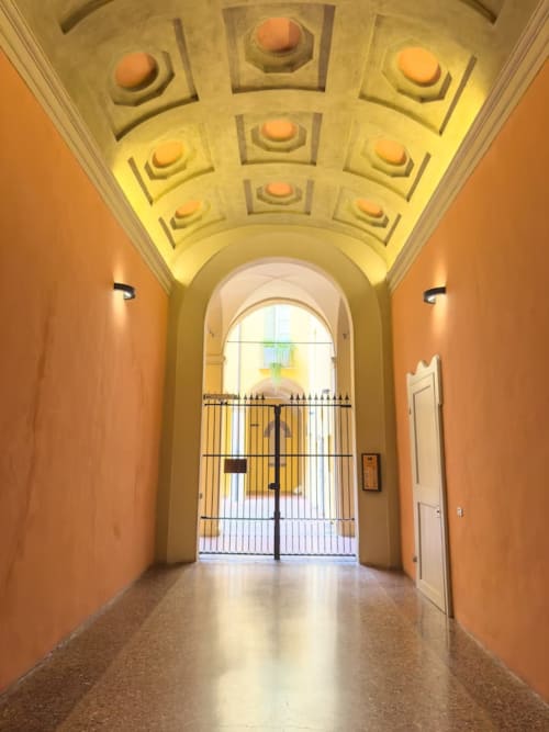 Elegante corridoio ad arco in palazzo storico bolognese con pareti in terracotta e soffitto riccamente decorato