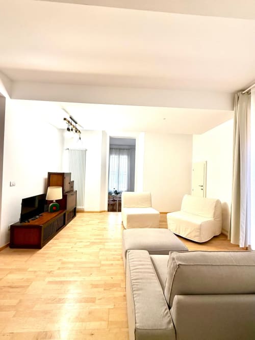 Ampio soggiorno dell'appartamento bolognese con divani color crema, pavimenti in legno, TV e arredamenti moderni