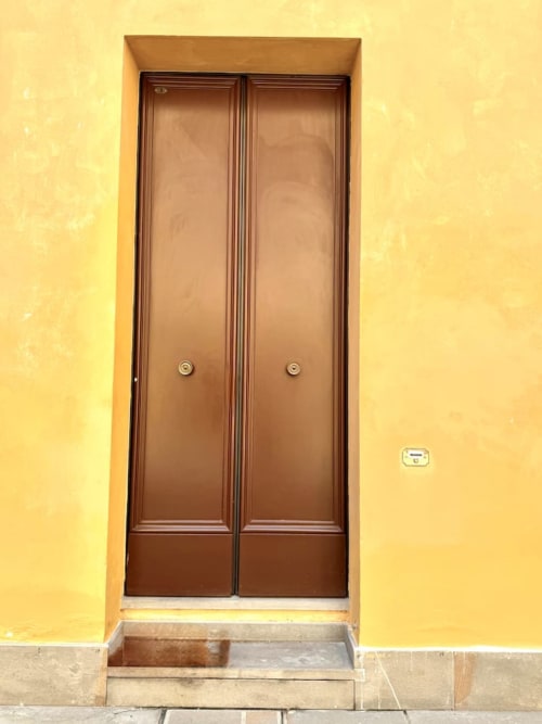 Doppio portone in legno marrone sulla facciata gialla di un storico appartamento bolognese a Living Palazzi Storici