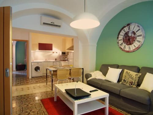 Moderno salón de apartamento con pared de acento verde, sofá, mesa de café blanca y cocina abierta en Cáceres