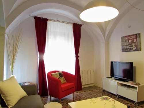 Luminoso salón en apartamento de Plaza de Santiago, Cáceres con sillón rojo, TV de pantalla plana, techo abovedado y vistas a la ciudad