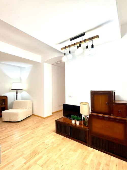 Soggiorno moderno nel palazzo storico bolognese con travi in legno, illuminazione contemporanea, arredi scuri e design minimalista