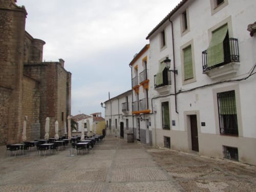 Plaza de Santiago histórica en Cáceres con edificios tradicionales blancos y amarillos, comedor al aire libre y arquitectura de piedra