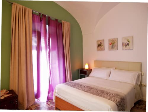 Dormitorio luminoso en apartamento Plaza de Santiago, Cáceres con paredes verde oliva, cortinas magenta, cama doble y papel tapiz floral