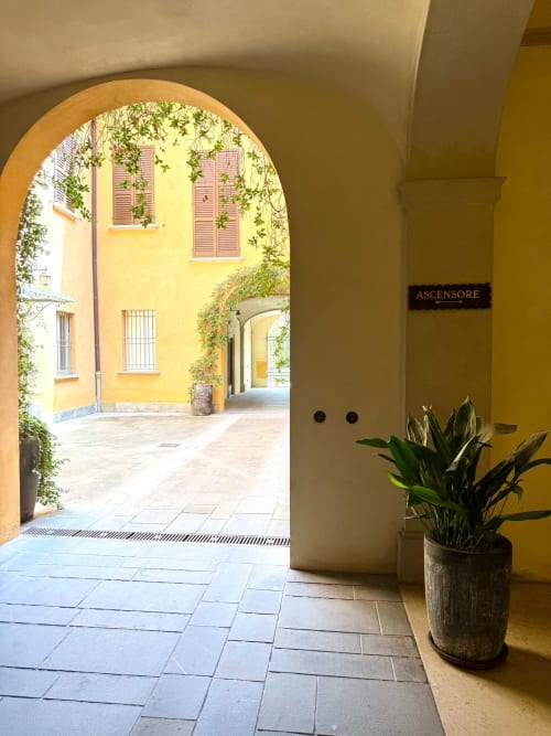 Corridoio palazzo giallo con passaggio ad arco e edera, ingresso appartamento Bologna con pianta in vaso