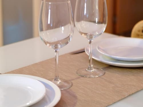 Elegante montaje de comedor en Apartamentos La Machacona con platos blancos, copas de vino y mesa de madera en apartamento de Cáceres.