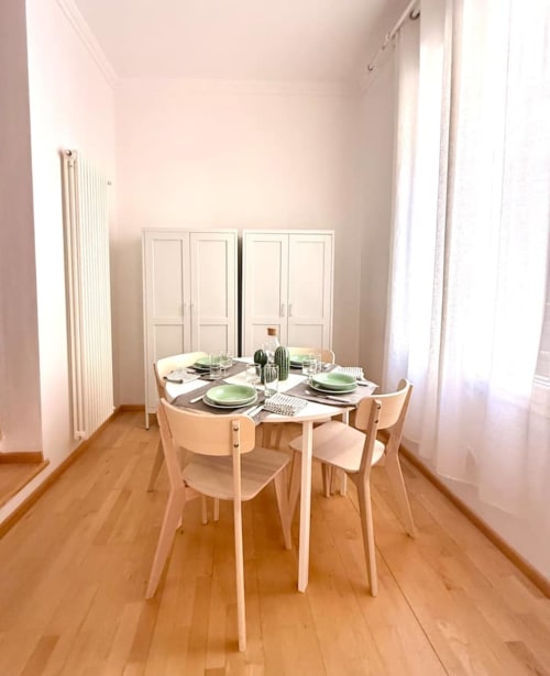 Sala da pranzo minimalista in appartamento bolognese con tavolo apparecchiato, sedie in legno e credenze color crema
