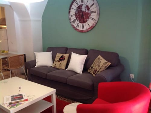 Sala moderna con sofá oscuro, sillón rojo, mesa de café blanca y reloj decorativo en apartamento Plaza de Santiago,