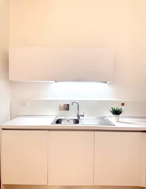 Angolo cottura minimalista con piano di lavoro bianco, lavandino e mobili crema in appartamento a Bologna