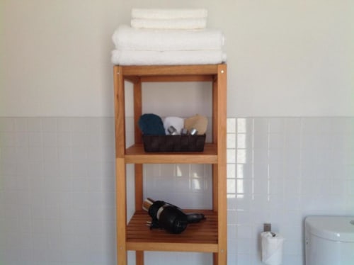Estantería de madera en baño con toallas blancas y artículos de aseo en apartamento La Machacona, Cáceres