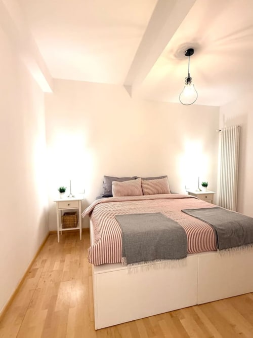 Camera da letto luminosa e moderna a Living Palazzi Storici Bologna con letto bianco, biancheria a righe rosa, pavimenti in legno e lampadario