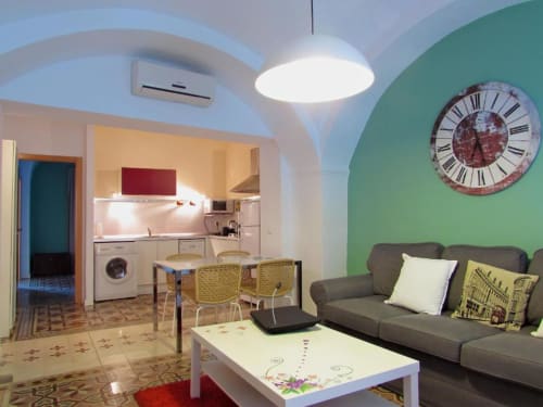 Sala de estar moderna en apartamento de Cáceres con sofá gris, pared verde, cocina y reloj vintage