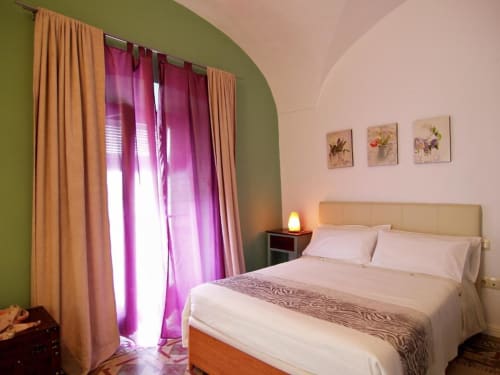 Dormitorio luminoso en apartamento Plaza de Santiago, Cáceres, con cama queen, pared verde, cortinas rosa y vistas a la ciudad