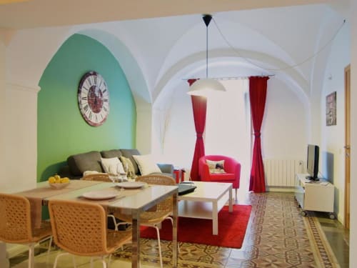 Moderno salón diáfano en apartamento Plaza de Santiago, Cáceres, con mesa de comedor, pared verde y asientos rojos