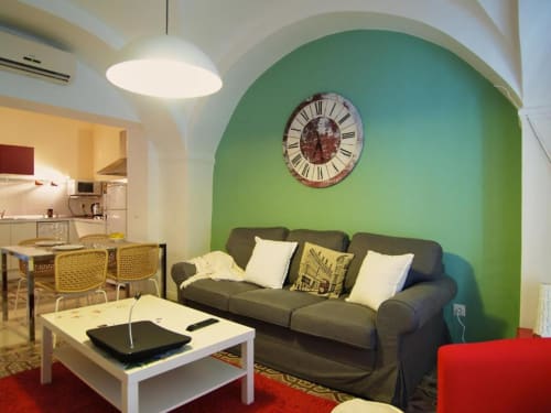 Sala de estar de apartamento moderno de 1 dormitorio en Cáceres con pared de acento verde, sofá oscuro y vistas a la ciudad