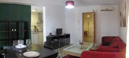 Sala de estar moderna en La Machacona, Cáceres con sofá rojo, mesa de comedor, TV y acceso a cocina