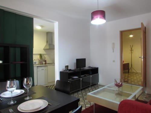 Zona abierta moderna de estar y cocina en apartamento de Cáceres con mesa de comedor, TV y lámpara colgante morada