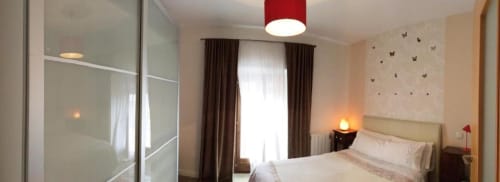 Dormitorio moderno en apartamento Plaza de Santiago, Cáceres, con cama doble, armario, cortinas marrones y lámpara de techo roja