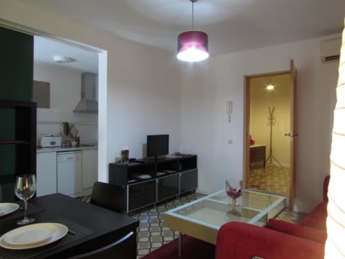 Amplio apartamento de planta abierta en Cáceres con cocina, comedor, sala de estar con TV, sofá rojo y acceso al pasillo