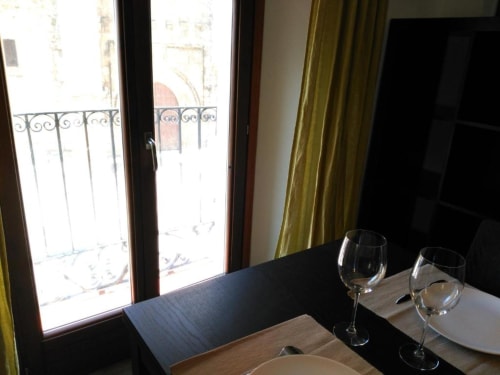 Mesa de comedor con copas de vino con vistas al balcón de la Plaza de Santiago en Apartamentos La Machacona, Cáceres