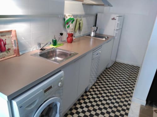Cocina moderna blanca con fregadero de acero inoxidable, lavadora, estufa y piso a cuadros blanco y negro en Apartamentos
