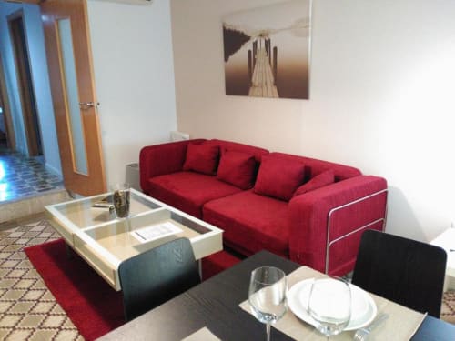 Sala de estar moderna en Cáceres con sofá rojo, mesa de comedor y obras de arte emblemático en Apartamentos La Machacona