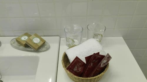 Amenidades del baño en La Machacona Cáceres: artículos de tocador, toalla blanca, vasos y jabones decorativos en canasta