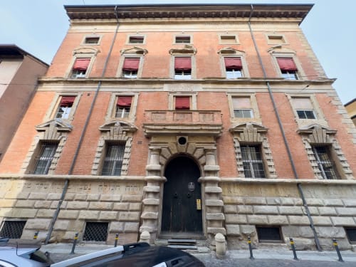 Historic red brick palazzo building in Bologna featuring arched entrance and period windows