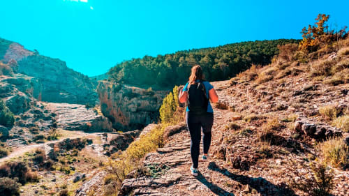 Mujer corriendo por senderos rocosos cerca de Bronchales con montañas boscosas bajo un cielo azul despejado