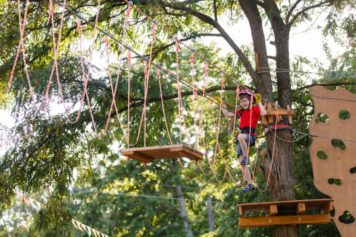 Niño en circuito de cuerdas entre árboles en el parque de aventura Casas rurales El abuelo y Lahuerta en Bronchales
