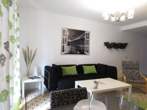 Sala moderna en apartamento de Cáceres con sofá negro, cojines verdes, mesa blanca y cuadro con vista a puente de la ciudad