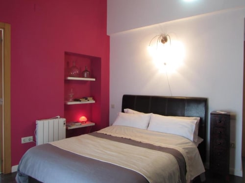 Dormitorio moderno con pared de acento rosa vibrante, cama con cabecera de cuero negro, estanterías integradas e iluminación contemporánea