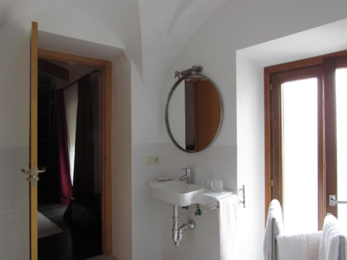 Baño moderno en apartamento de Cáceres con espejo redondo, lavamanos blanco, puertas de madera y luz natural abundante