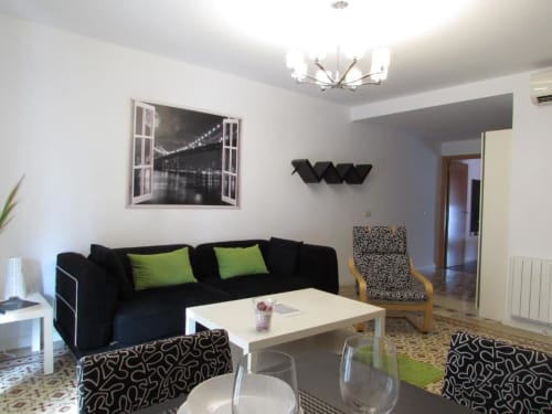 Moderna sala de estar del apartamento La Machacona en Cáceres con sofá negro, cojines verdes, mesita blanca y vistas al puente de la ciudad