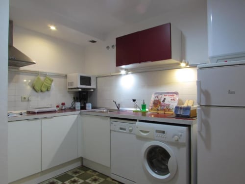 Cocina moderna en apartamento de Cáceres con muebles blancos, armarios superiores burdeos, electrodomésticos de acero inoxidable y lavadora