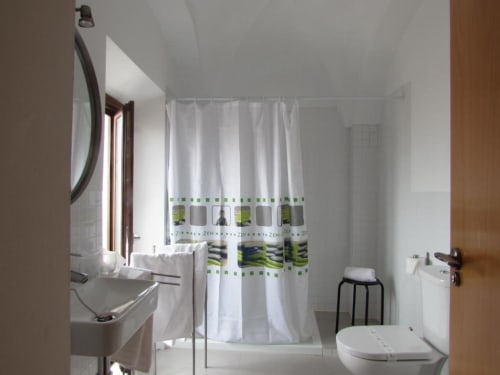 Baño moderno en apartamento de Cáceres con cortina de ducha blanca, lavabo, inodoro y suelo de baldosas