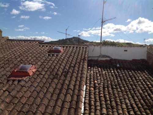Tejados de tejas de barro de edificios históricos de Cáceres con vistas de la ciudad y torres de antena bajo cielo azul