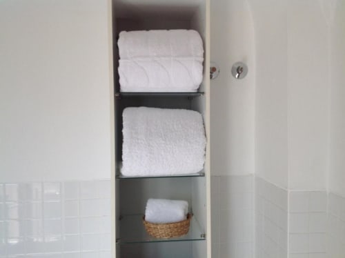 Armario de baño empotrado con toallas blancas y paños de mano apilados en estantes, almacenamiento en cesta tejida en Apartamentos La