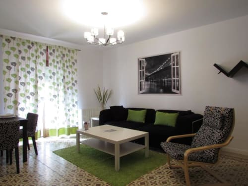 Moderno salón en apartamento de Cáceres con sofá negro, detalles verdes y vistas a la ciudad
