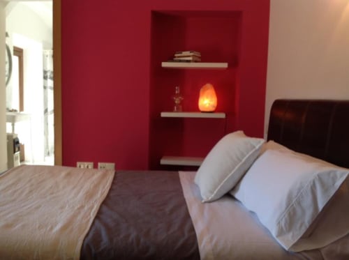 Dormitorio moderno en Apartamentos La Machacona, Cáceres, con pared roja acentuada, cama doble, almohadas blancas y lámpara iluminada