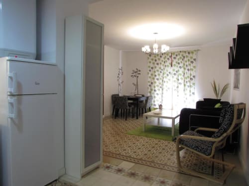 Moderna zona de estar diáfana en apartamento Plaza de Santiago, Cáceres, con cocina blanca, sofá negro, mesa de comedor y verde