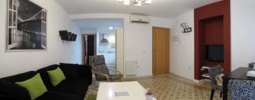 Amplia sala de estar en apartamento Plaza de Santiago, Cáceres, con sofá negro, cojines lima y pared roja con TV