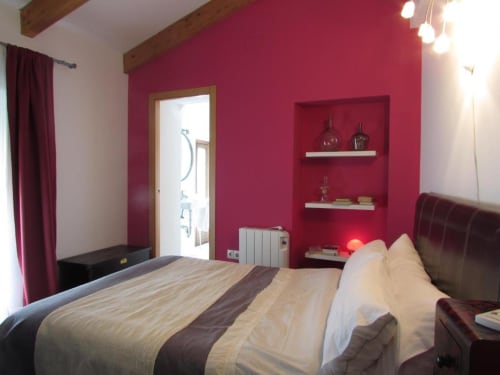 Habitación moderna en Apartamentos La Machacona con paredes rojo vibrante, ropa de cama blanca, vigas de madera y estantes