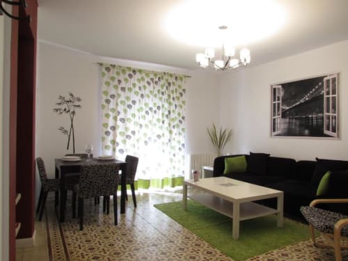 Sala moderna con sofá negro, detalles verdes, comedor y cortinas de balcón en apartamento Plaza de Santiago, Cáceres
