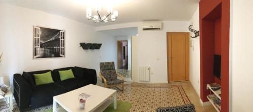 Moderna sala de estar en Apartamentos La Machacona de Cáceres con sofá negro, mesa blanca y pared de acento rojo
