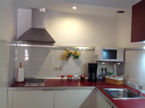 Cocina moderna en apartamento Plaza de Santiago de La Machacona, Cáceres con encimeras rojas, gabinetes blancos y acero inoxidable