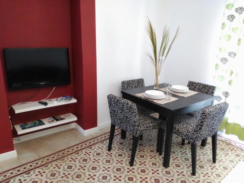 Comedor moderno del apartamento La Machacona en Cáceres con mesa negra, sillas estampadas y pared roja de acento