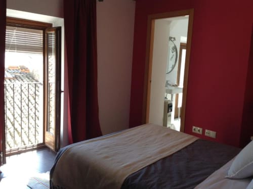 Dormitorio moderno en Apartamentos La Machacona, Cáceres, con paredes rojas, balcón con vistas a la ciudad y mobiliario contemporáneo